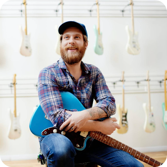 A seated man holds a blue electric guitar